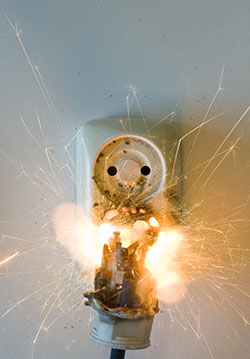 A malfunctioning plug exploding from a wall socket in a flash of electricity.