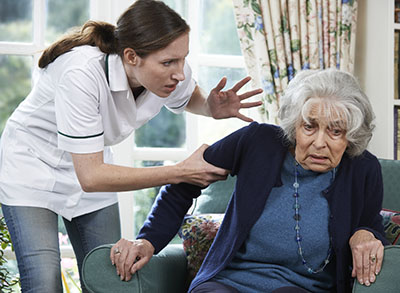 A nursing home carer aggressively grabs an elderly woman's arm.