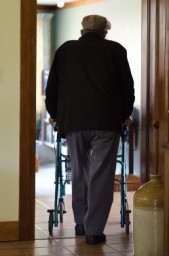 an older man walks with assistance after a brain injury.