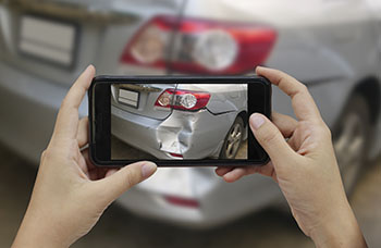 A person using their phone to take a picture of damage to the rear bumper of a car