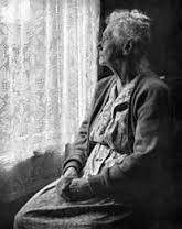 an elderly woman sits alone looking out the window.