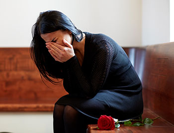 A grieving woman sits with her face in her hands at the funeral of a loved one.