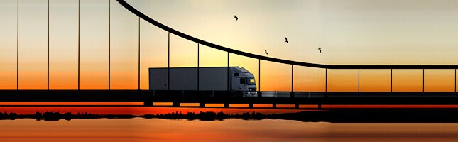 A large semi truck crossing a bridge in front of a picturesque sunset